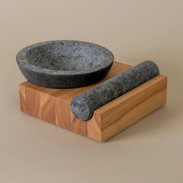 Stone mortar and pestle set on a wooden base against a beige background