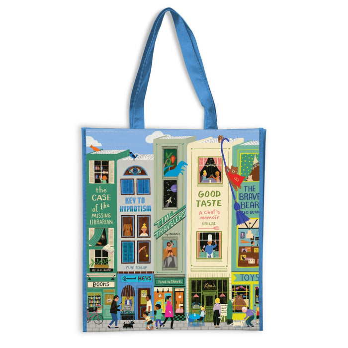 The Main Street Books Reusable Shopping Bag by Anne Bentley features blue handles and vibrant artwork of storefronts, apartments, a bookshop, toy store, cafΓ©, plus people and animals bringing the lively street scene to life.