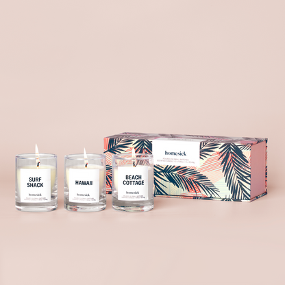 Three mini candles labeled "Beach Cottage", "Hawaii", and "Surf Shack" in front of a box on a cream background