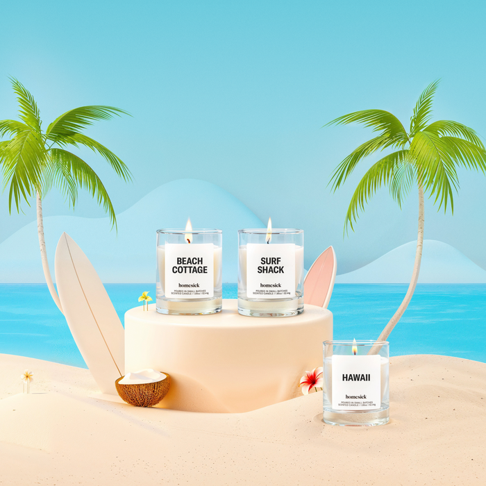 Lifestyle image of three mini candles labeled "Beach Cottage", "Hawaii", and "Surf Shack" in a beach vacation setting