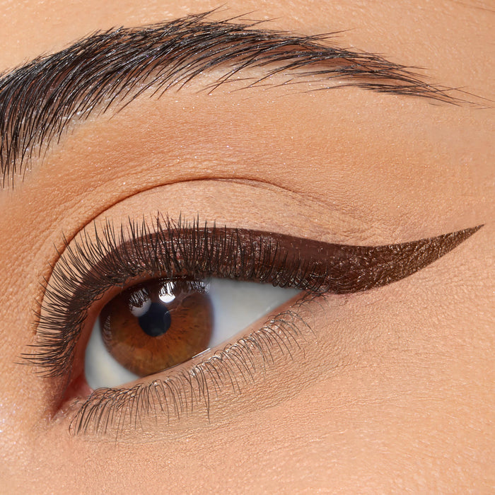 Winged eyeliner defines the upper lash line in a sharp, deep-brown cat eye, created with ColourPop BFF Liquid Liner in Grande, on a close-up of a brown eye with soft nude shadow and a groomed brow.