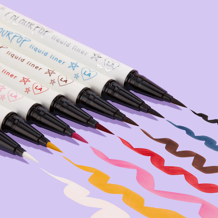 ColourPop Graceland BFF Liquid Liner creates a bold white squiggle beside multicolor swatches, the felt‑tip pen and doodled white barrel angled on a lavender background, showcasing precise application and opaque, quick‑dry wear.