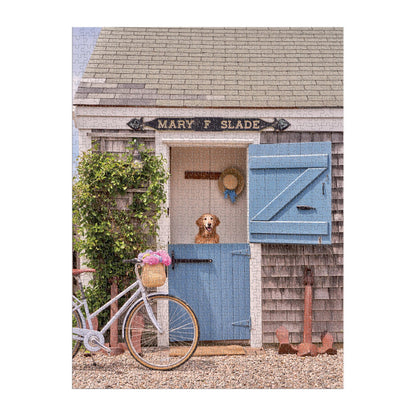 A brown and white dog stands in a Dutch doorway of a small wooden building, with a bike and flowers nearby—captured in the Gray Malin Nantucket 1000 Piece Book Box Puzzle by Gray Malin.