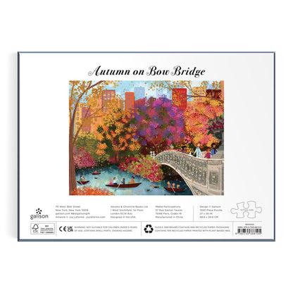 The Joy Laforme Autumn on Bow Bridge 1000 Piece Puzzle displays an autumn scene of Central Park’s Bow Bridge, colorful trees, and boaters, with “Autumn on Bow Bridge” above the illustration and Joy Laforme branding below.