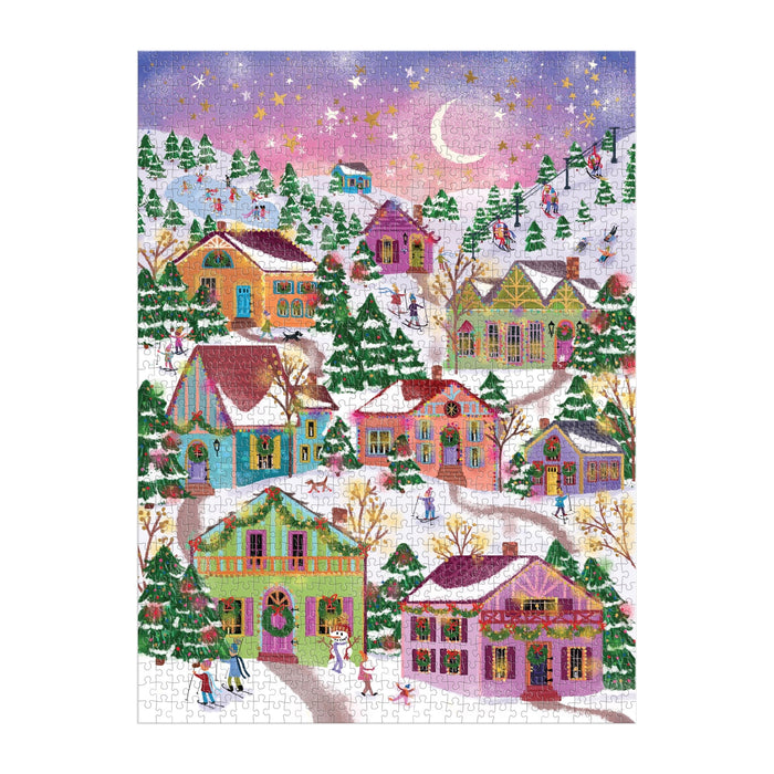 The Joy Laforme Snowcap Village 1000 Piece Foil Puzzle showcases a vibrant winter village scene with festive foil accents, snow-covered houses, pine trees, and people strolling under a crescent moon at sunset.