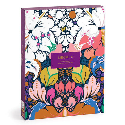 The Liberty London Liberty 9 x 12 Paint by Number Kit Glastonbury features a vibrant floral design in pink, blue, green, yellow, orange, white, and purple with a central purple label and premium acrylic paints.