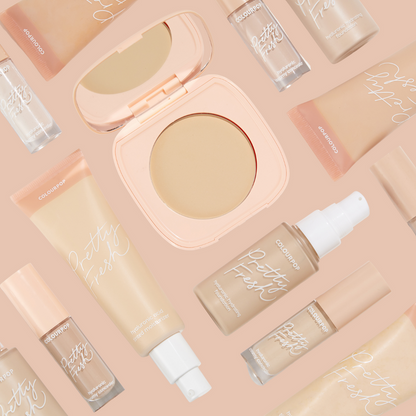 Fair 1 N shade of ColourPop Pretty Fresh Tinted Moisturizer rests in a beige squeeze tube with white pump among matching Pretty Fresh concealer, setting spray, and powder compact on a peach backdrop, highlighting its hyaluronic acid formula.