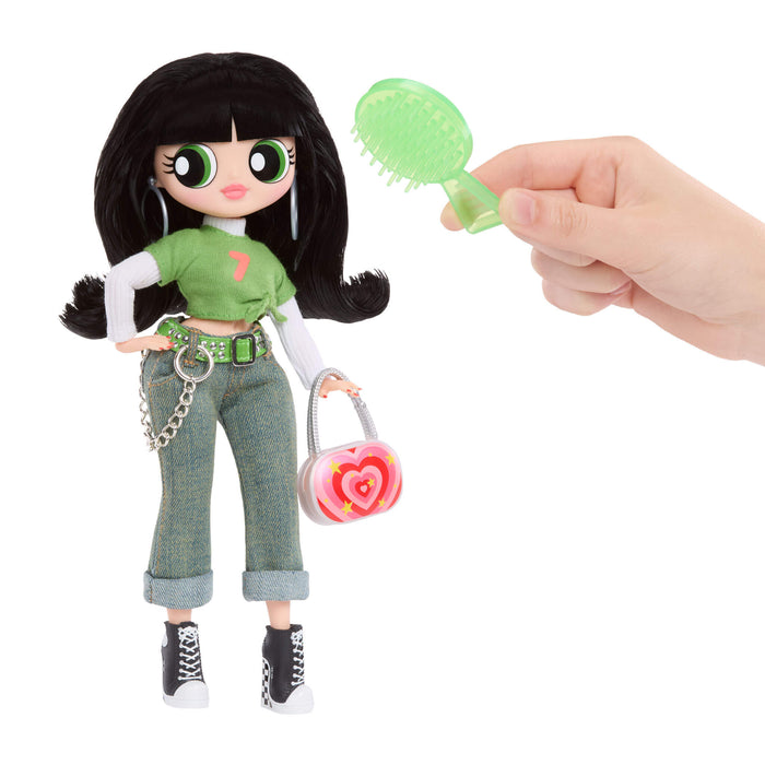 Toy doll with black hair and green outfit holding a small pink bag, with a hand holding a green comb.