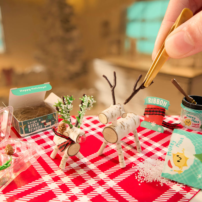 Mini reindeer figurines on a red and white checkered tablecloth with a blurred indoor background.