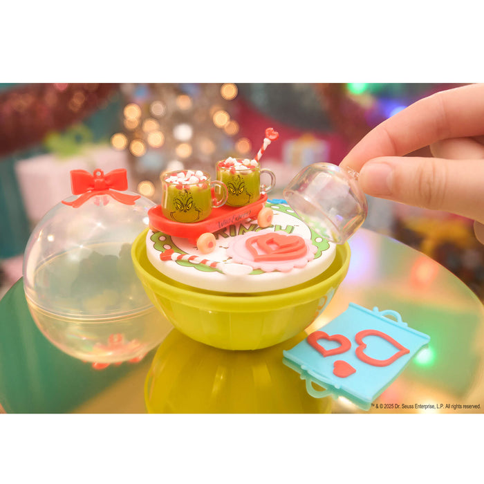 Mini Grinch cups with a green base on a reflective surface with blurred lights in the background.