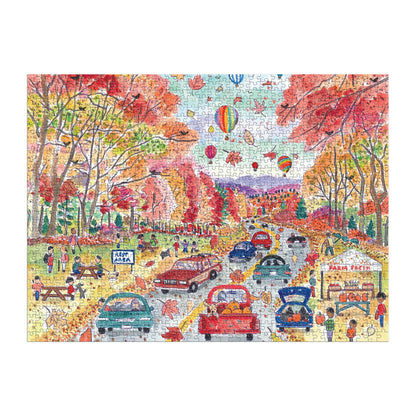 The Michael Storrings Leaf Peeping 1000 Piece Puzzle by Michael Storrings showcases cars, people enjoying outdoor fun, picnic tables, a food stand, and hot air balloons floating over scenic autumn foliage.