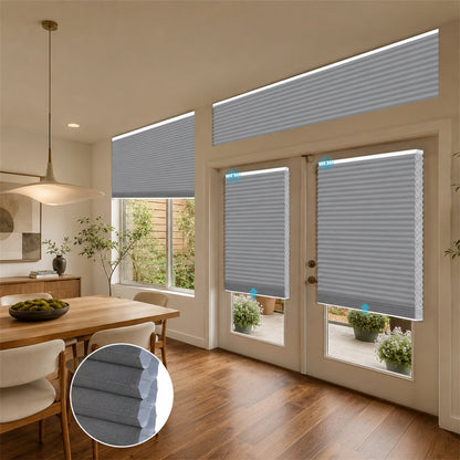 Gray cellular window and door blinds installed in a modern dining room and patio area, with an inset circular detail of the fabric texture.