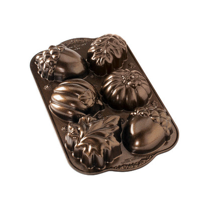 A dark brown cast iron loaf pan with decorative autumn-themed molds shaped like acorns, pumpkins, and leaves, shown on a plain white background.