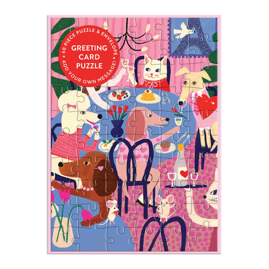 Colorful cats and dogs gather around a flower-adorned table on a pink and purple background in the completed Anne Bentley Paws for Love Greeting Card Puzzle.