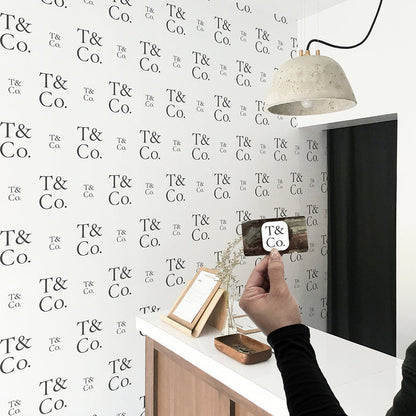 A wall in a business featuring a step-and-repeat wallpaper print created by Tempaper, prominently displaying the company's logo, with a person holding a business card that features the same logo.