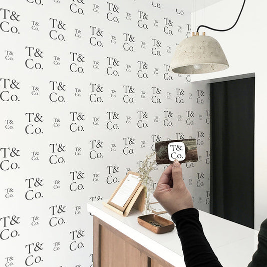 A wall in a business featuring a step-and-repeat wallpaper print created by Tempaper, prominently displaying the company's logo, with a person holding a business card that features the same logo.