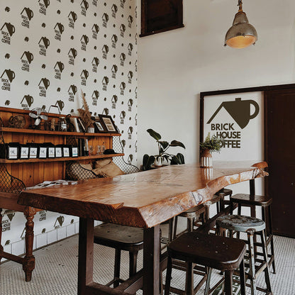 A wall in a coffee shop featuring a step-and-repeat wallpaper print created by Tempaper, prominently showcasing the coffee shop's logo