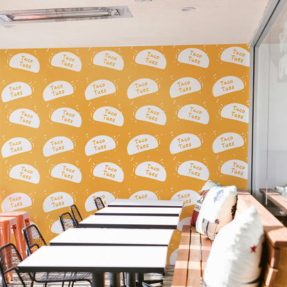 A wall in a shop featuring a step-and-repeat wallpaper print created by Tempaper, prominently showcasing the shop's 'Taco Tues' logo.