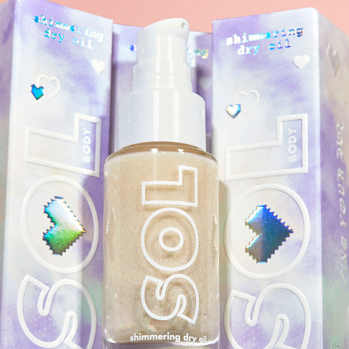 Rainbow Glow SOL Shimmering Dry Oil bottle pumps out golden, sparkly body oil, set against iridescent lavender packaging with holographic hearts; ColourPop SOL Shimmering Dry Oil for a radiant, sunlit glow.