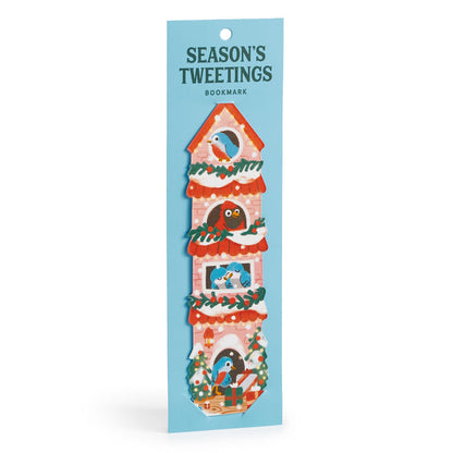 A festive Seasons Tweetings Paper Bookmark by Éléna Comte features a tall red birdhouse with garlands, birds, and gifts, attached to blue packaging—a perfect holiday reading accessory.