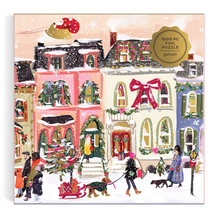 Nysha Lilly’s “Snowfall on Main Street 1000 Piece Foil Puzzle” features a festive winter scene with people, pets, colorful homes, Santa’s sleigh overhead, a big red bow on a house, and shimmering foil accents on the gold label.