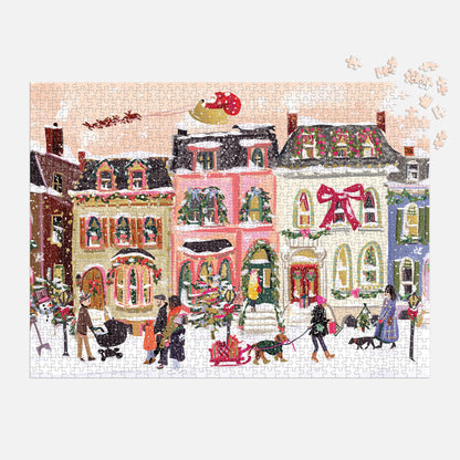 Nysha Lilly’s Snowfall on Main Street 1000 Piece Foil Puzzle showcases a festive winter street with decorated houses, children playing, and Santa’s sleigh overhead—just a few sparkling foil pieces remain to complete it.