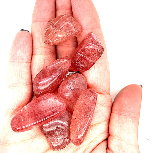 A group of Strawberry Quartz tumble gemstone in a models palm on a white background, front view.