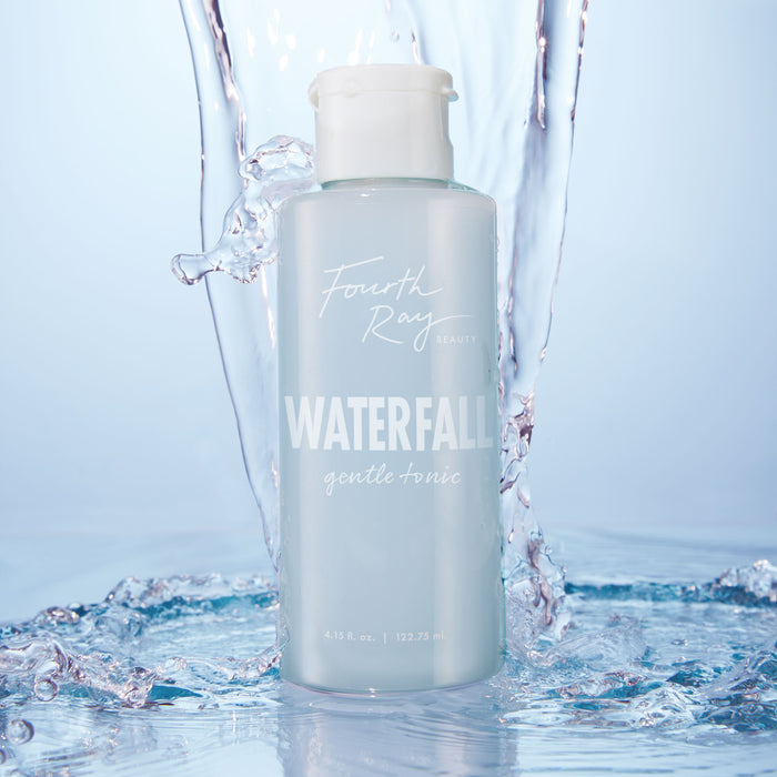 Fourth Ray Beauty Waterfall Gentle Tonic face toner standing upright as water splashes around it, showcasing a pale blue 4.15 fl oz bottle with white flip cap; hydrating ColourPop Face Toner in a fresh waterfall setting.